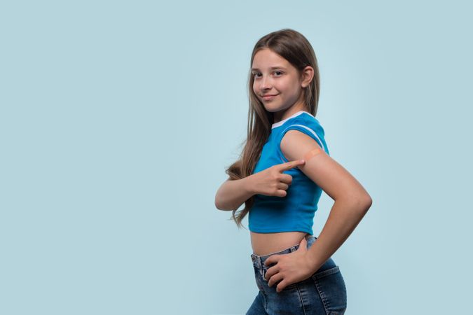 Girl confidently pointing at bandage on arm after vaccination