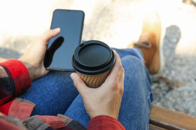 Woman in jeans and shirt hold paper cup and phone outdoor