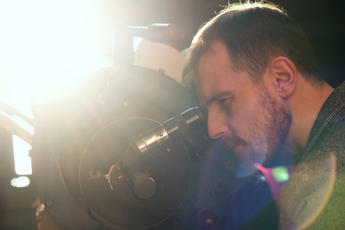 Bearded man examines the sky through telescope lens.