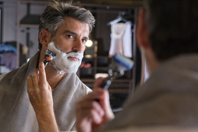Mature male shaving beard against mirror
