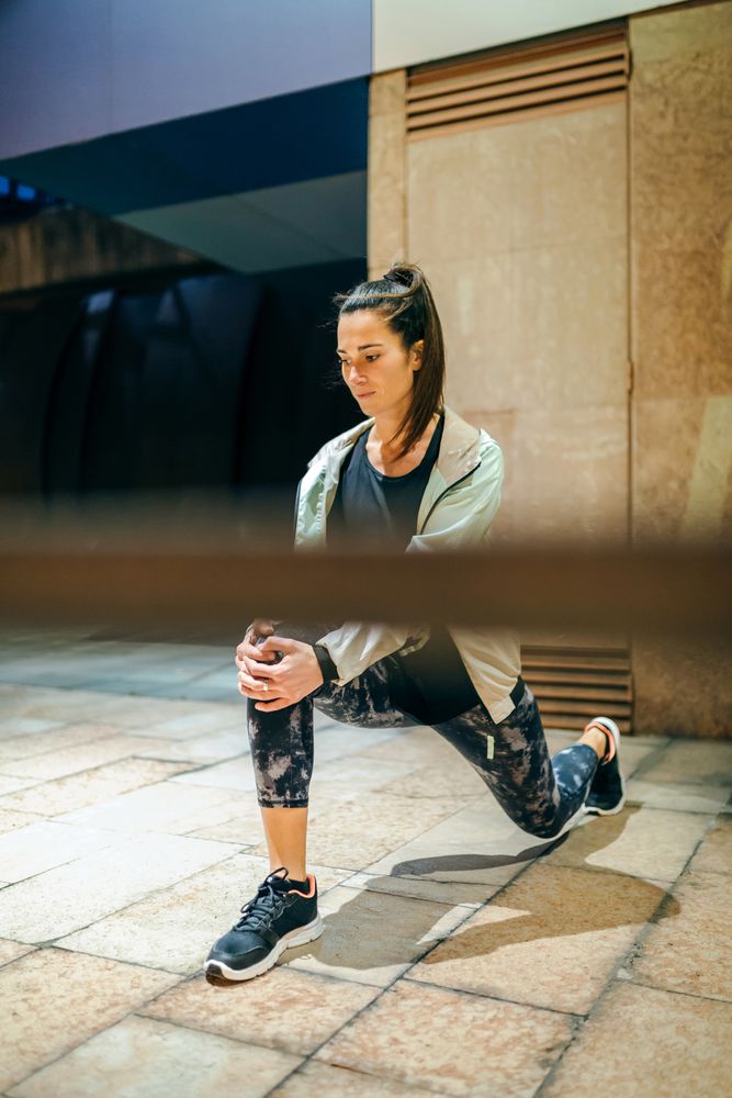 Woman runner stretching her legs behind banister before training at night in town