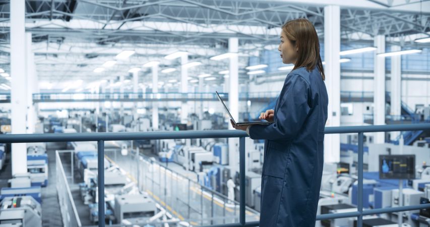 Electronics Manufacturing Technician Working on a Laptop Computer at a Factory Space. Asian Female Specialist Developing, Maintaining, Fine-Tuning Programs for Machine Production and Assembly