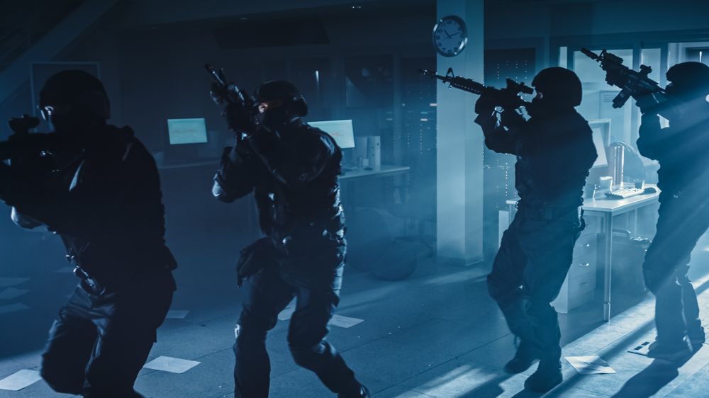 Masked Squad of Armed SWAT Police Officers Move in a Hall of a Dark Seized Office Building with Desks and Computers.