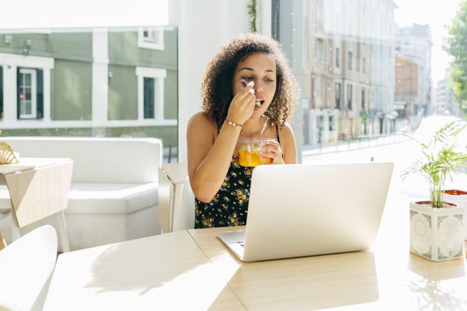 hispanic female with laptop enjoying healthy drink in cafe