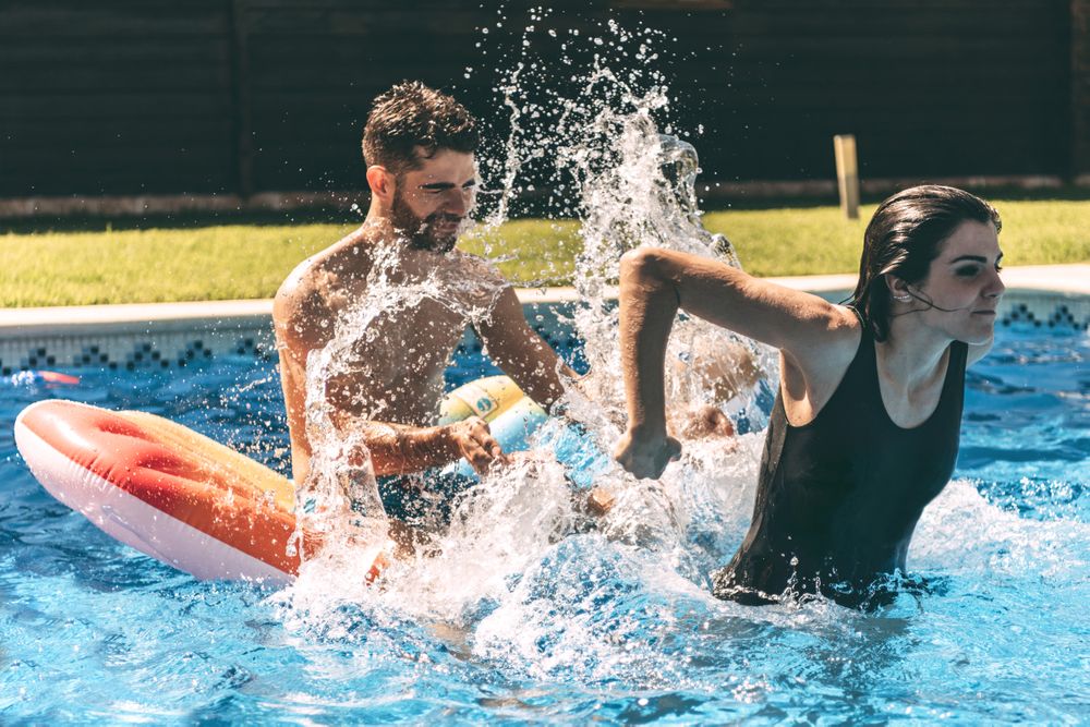 Young woman splashing on man sitting on airbed in the pool