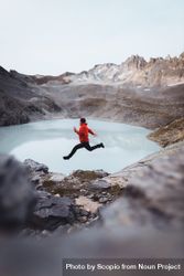 Side view of a man in red jacket jumping beside frozen lake in the mountain in Switzerland 4dMPDb