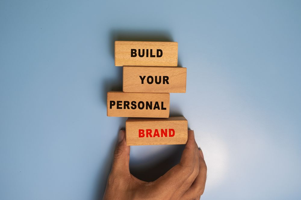 male hand put a wooden blocks with build your personal brand words isolated on blue background