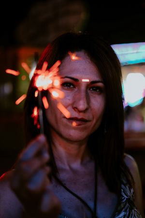Woman holding sparkler on fairground in evening