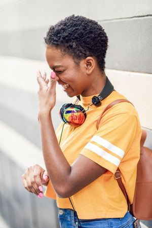 Laughing Black woman with headphones in front of grey striped wall