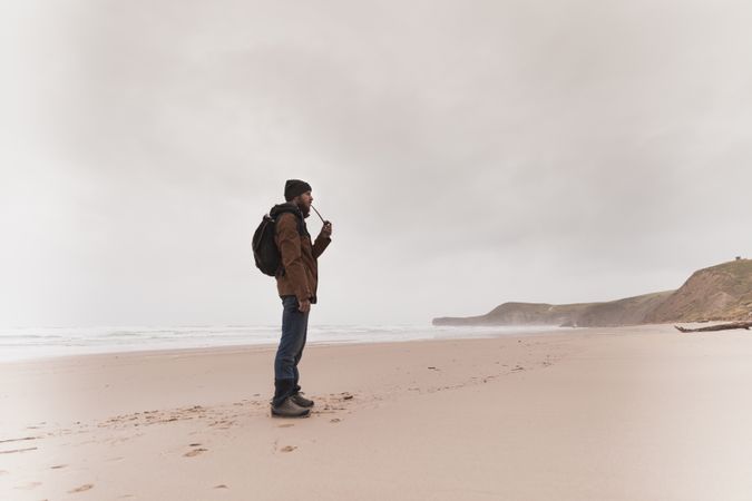 Man smoking pipe on sand shore near water