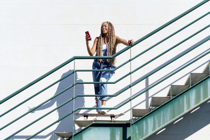 Laughing female skater standing and using phone on stairs, copy space