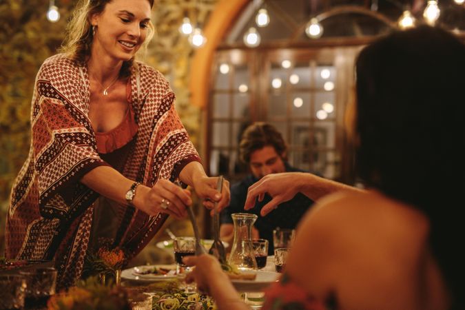 Woman serving food to friends at dinner table