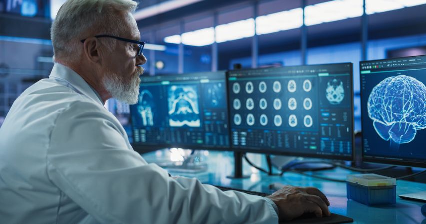 Cancer Research Center Medical Laboratory: Male Neuroscientist Using Desktop Computer To Analyze CT Scans Of Human Brain.
