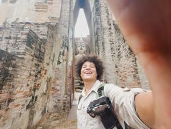 Joyful selfie capturing a traveler with smartphone and Buddha statue