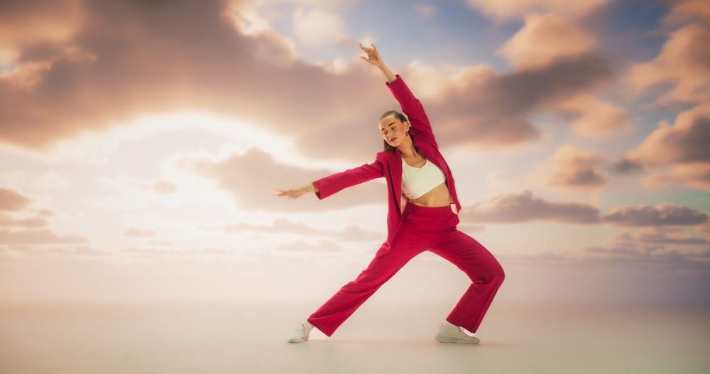 Athletic Woman in Stylish Outfit Dancing Energetically in Studio with Sky Background. Creative Female Performing Contemporary Dance Choreography On Set During Virtual Production