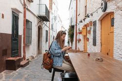 Young woman in small village sitting at outside wood table looking at cell phone