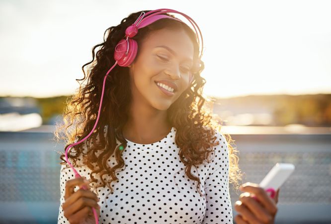 Woman wearing pink headphones enjoying listening to something on her phone