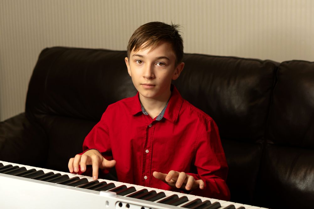 Boy looking at camera while playing digital piano.