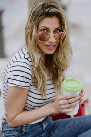 Happy woman with disposable cup of coffee sitting on street bench