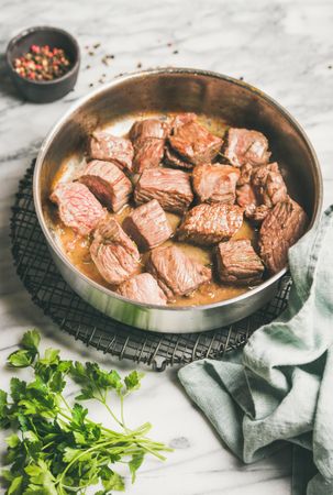 Chunks of braised beef in pan, with parsley and peppercorn