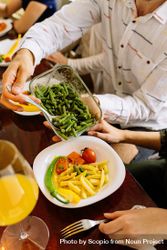 Cropped image of person holding green vegetable dish sitting at dinner table 5lKoa0