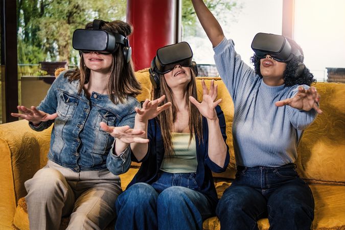 Three female friends in VR headsets on yellow sofa