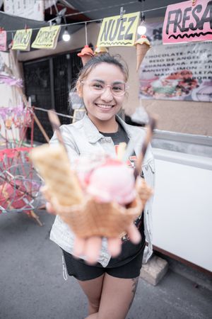A young Hispanic woman is smiling holding a traditional ice cream in front of a street market stall