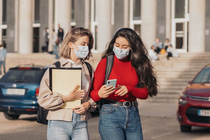 Two students with mask watching the mobile in the college