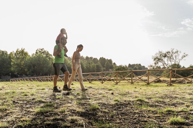 Father carrying daughter on shoulders while walking with mom on countryside path