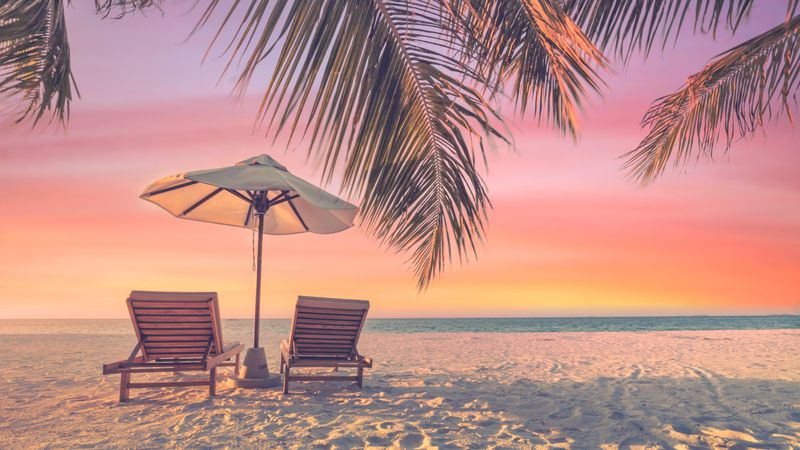 Beautiful gradient sunset with two reclining chairs and parasol