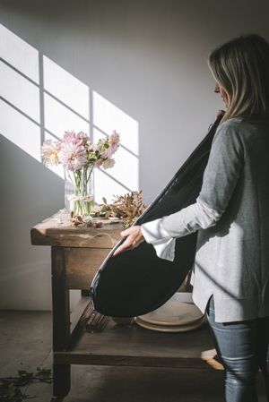 Woman with case near bunch of flowers in vase between dry leaves on table