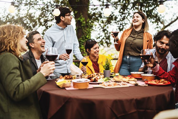 Group of multi-ethnic carefree friends talk, joke and drink wine during the brunch of a harvest wine tasting