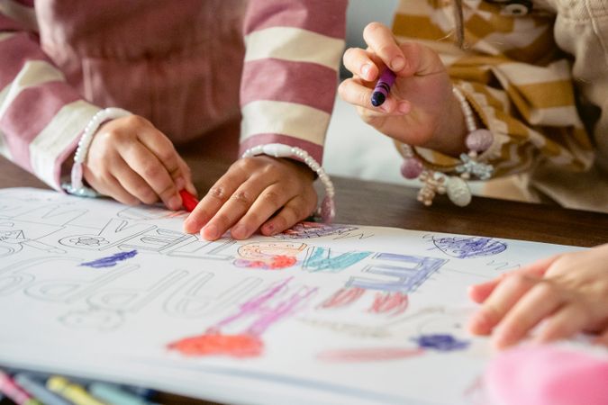 Cropped image of a child and adult drawing and coloring with crayon