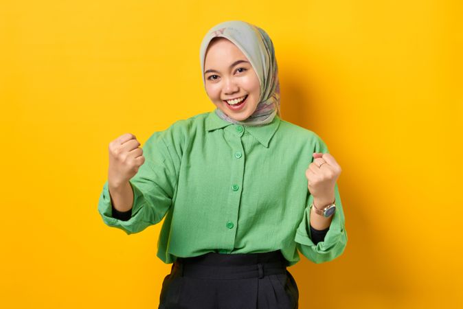 Smiling Muslim woman in headscarf and green blouse with both hands in celebratory fists