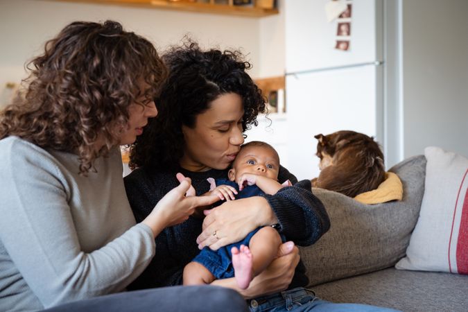 Two new moms on sofa holding their baby lovingly