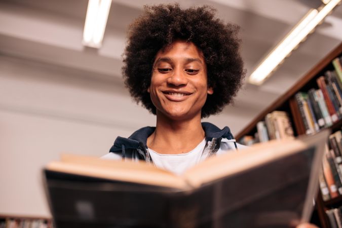 Young biracial student smiling and reading textbook