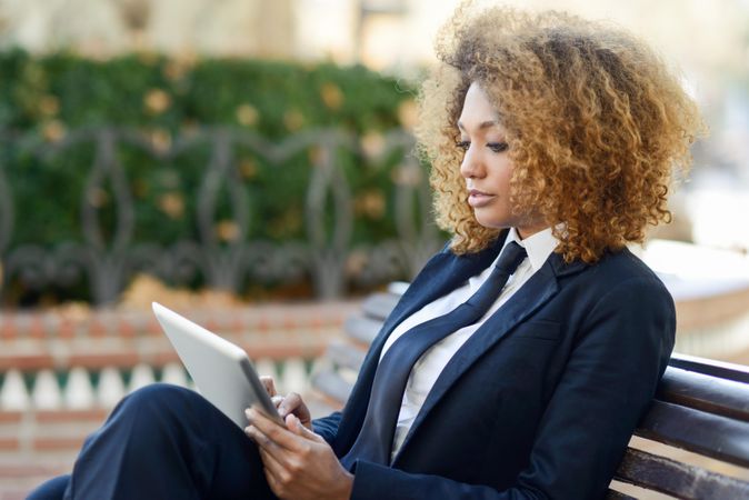 Woman in suit looking intently at something on her digital tablet’s screen while sitting outside