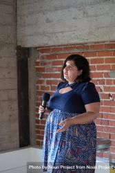 Woman holding a microphone giving a talk with an exposed brick wall behind her 5poLe0