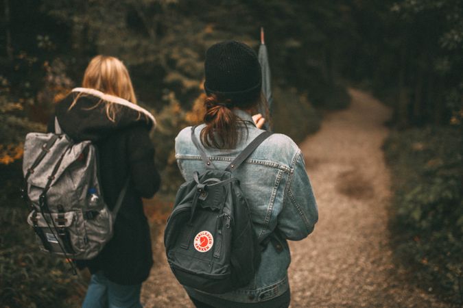 Back view of two young women with backpacks walking in the woods