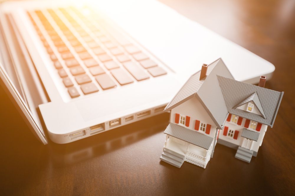 Miniature House And Laptop Computer Resting on Desktop.
