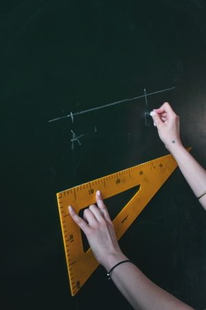 Cropped image of math teacher holding square frame ruler on chalk board