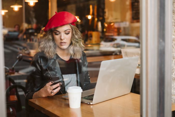 Woman with laptop using smartphone in cafe