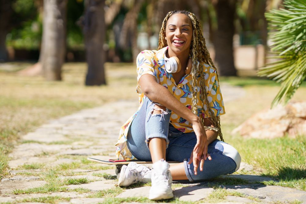 Smiling female sitting on skateboard walkway in park