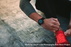Close up of hands of a fitness man wearing a digital wrist watch tying shoe laces 4Mpna5