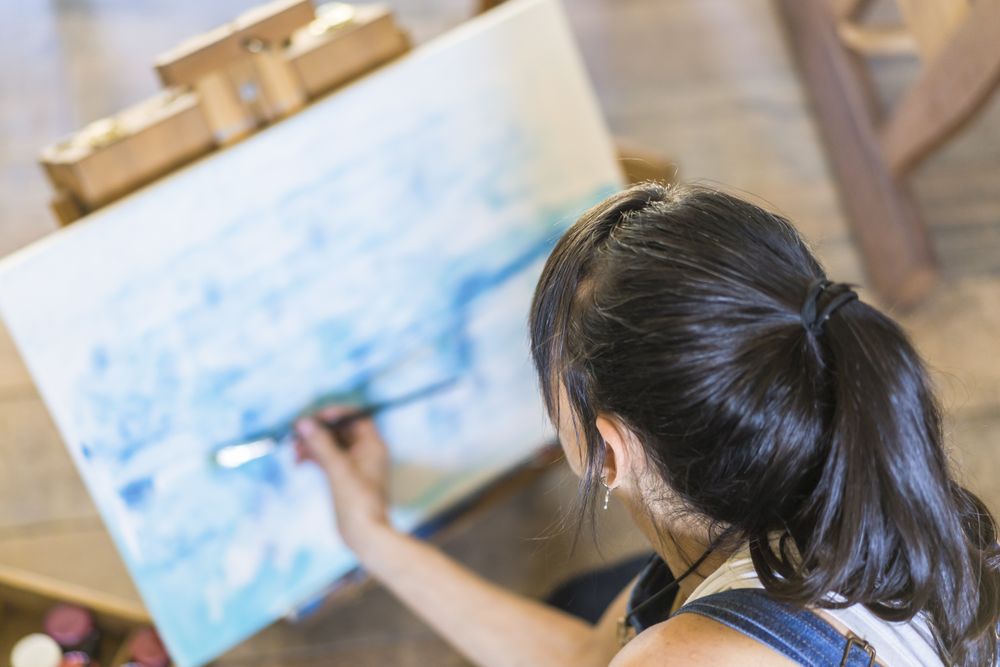 Woman artist painting on a canvas a blue abstract painting. Creative ywoman working on the floor in her art studio.