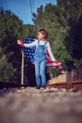Child standing on railroad with flag of America in summer