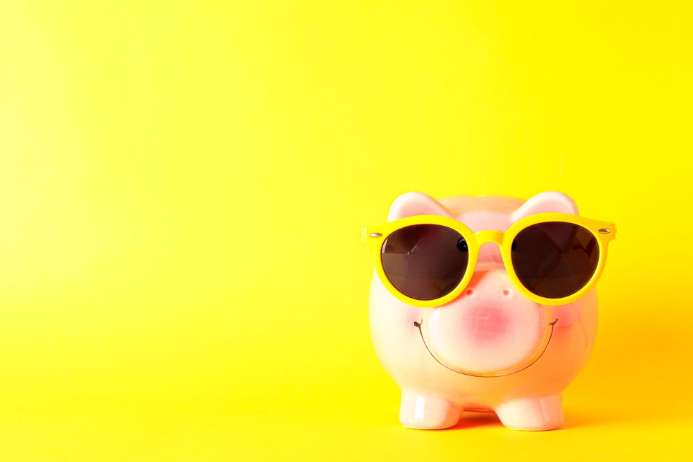 Happy piggy bank with sunglasses on yellow background, space for text. Finance, saving money