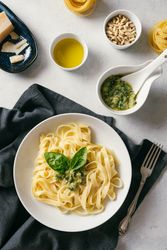 Served plate of pesto pasta next to bowl of sauce on table