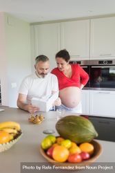 Pregnant woman and male partner deciding what to cook for dinner from recipe book 4ByPx5