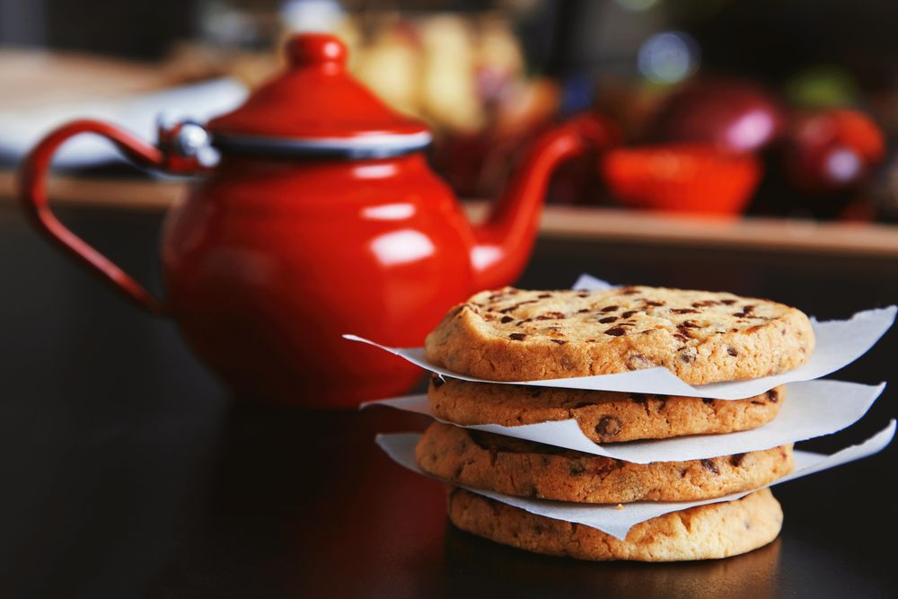 Shiny red tea pot on kitchen table with pile of cookies